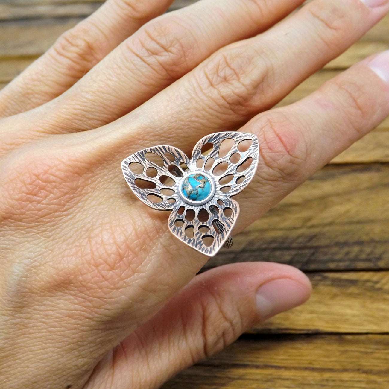 Front view of a copper and sterling silver flower ring featuring a copper turquoise gemstone, worn on a finger.
