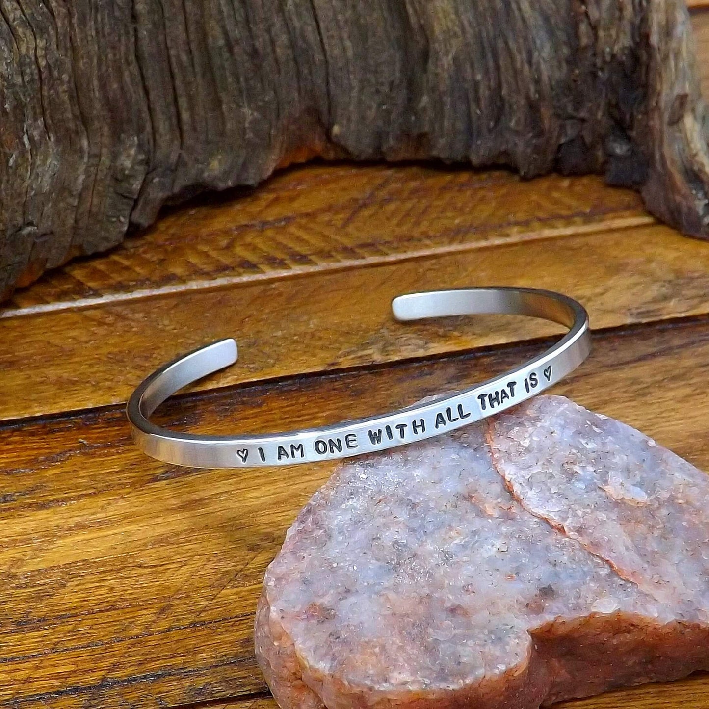 Left side view of a sterling silver affirmation cuff bracelet hand-stamped with "I AM ONE WITH ALL THAT IS".