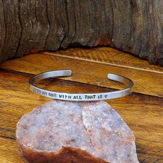 Right side view of a sterling silver affirmation cuff bracelet hand-stamped with "I AM ONE WITH ALL THAT IS".