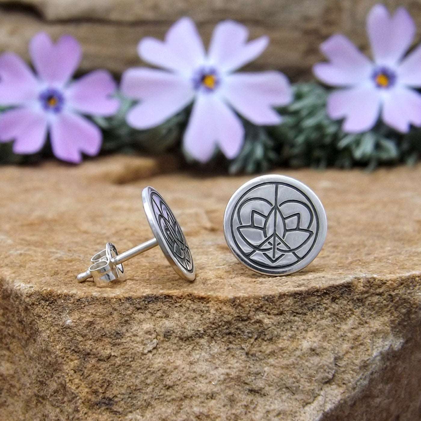 Side view of a pair of sterling silver stud earrings hand-stamped with large Jenn's Zen Creations logo.