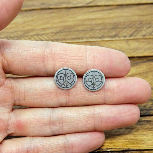 Size reference view of a pair of sterling silver stud earrings hand-stamped with large Jenn's Zen Creations logo.
