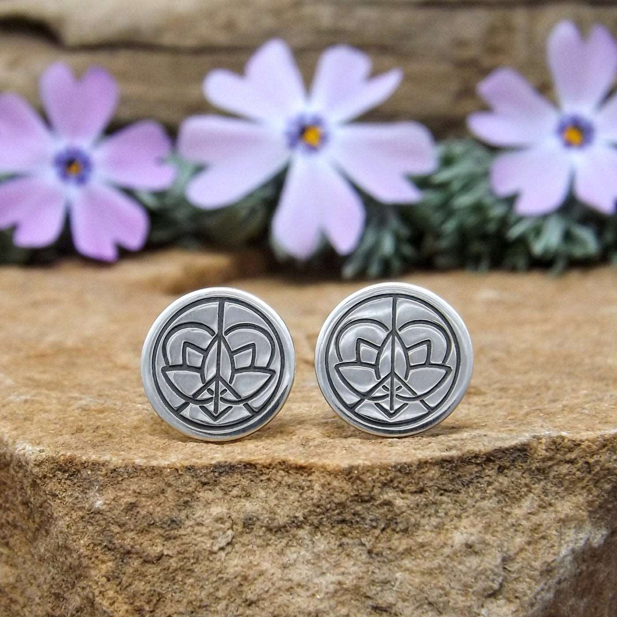 Front view of a pair of sterling silver stud earrings hand-stamped with large Jenn's Zen Creations logo.