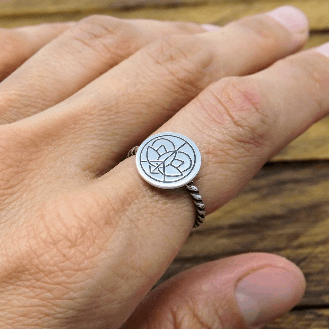 Sterling silver twist wire band ring with large Jenn's Zen Creations hand-stamped logo, worn on a finger.