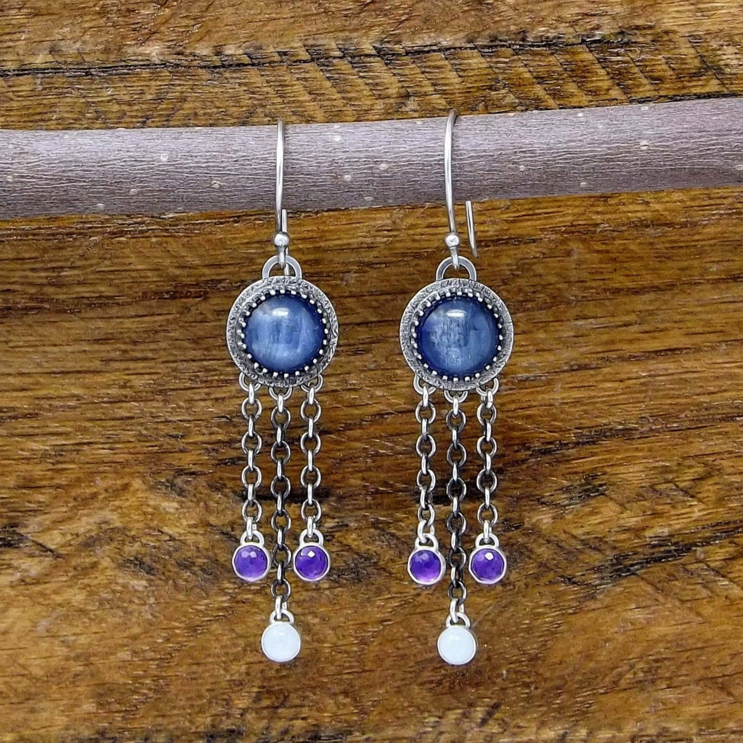 Front view of a pair of sterling silver dangle earrings featuring kyanite, rainbow moonstone, and rose cut faceted amethyst gemstones. Heart designs adorn the back of the earrings.