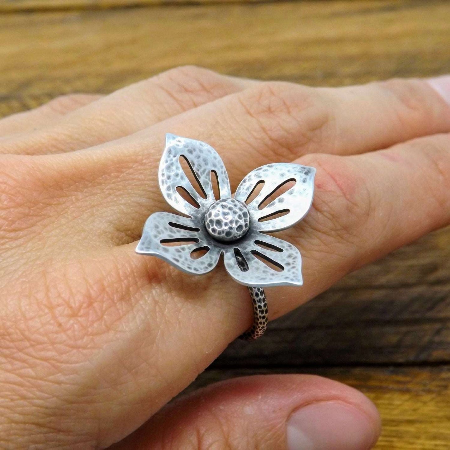 View of a one-of-a-kind argentium and sterling silver flower ring, worn on a finger.