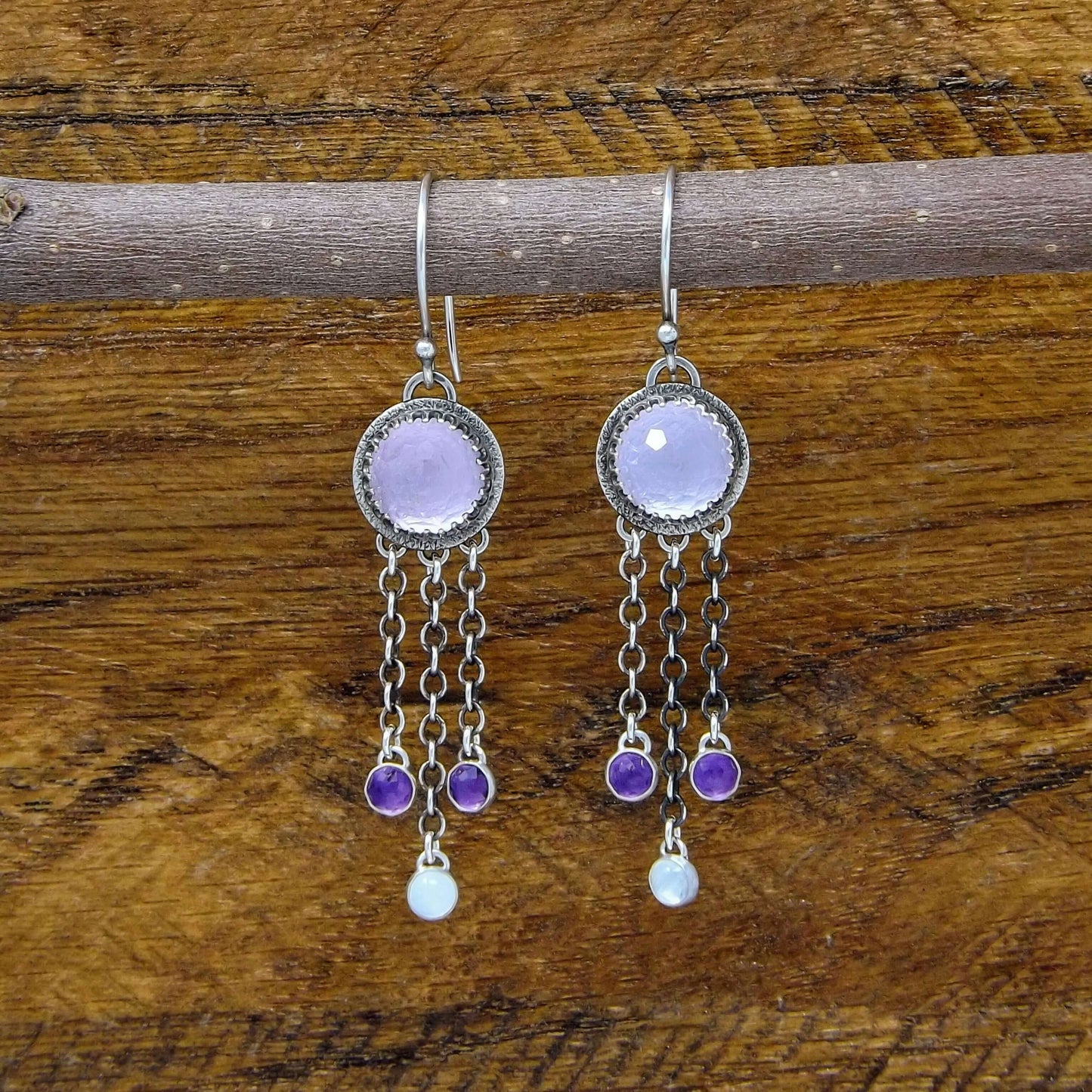 Front view of a pair of sterling silver dangle earrings featuring rose cut faceted amethyst and rainbow moonstone gemstones. Heart designs adorn the back of the earrings.