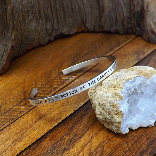 Left side view of a sterling silver affirmation cuff bracelet hand-stamped with "I AM A REFLECTION OF THE BEAUTY & WONDER OF THE UNIVERSE".