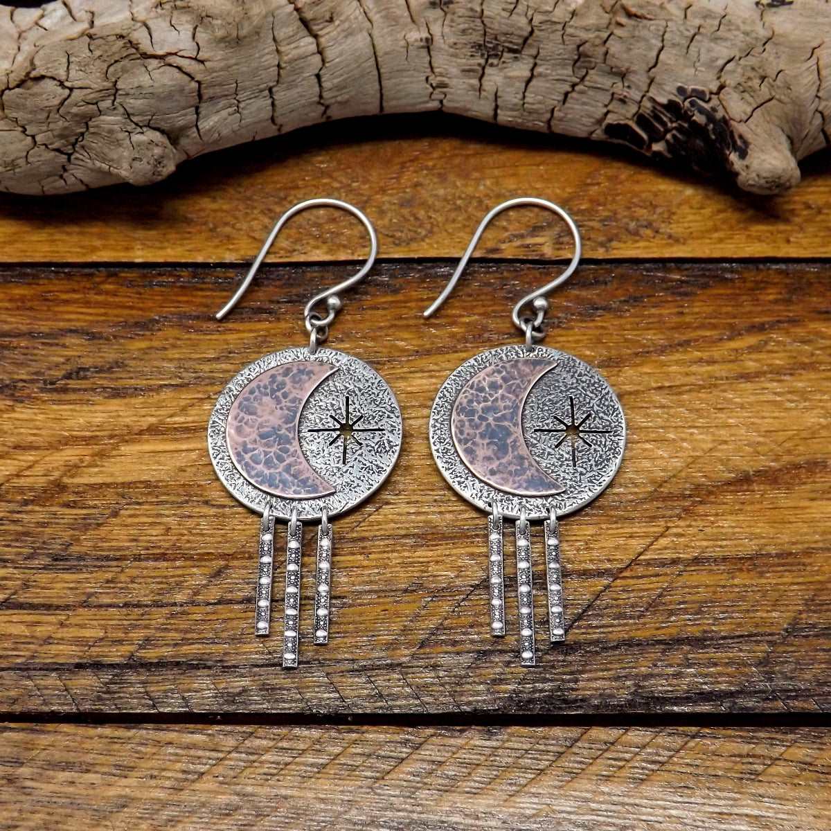 Front view of a pair of sterling silver dangle earrings adorned with a copper crescent moon and star.