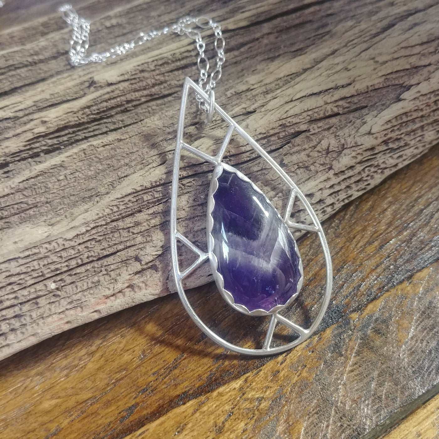 Left angle view of an argentium silver necklace with a geometric design and featuring a teardrop shaped chevron amethyst gemstone.