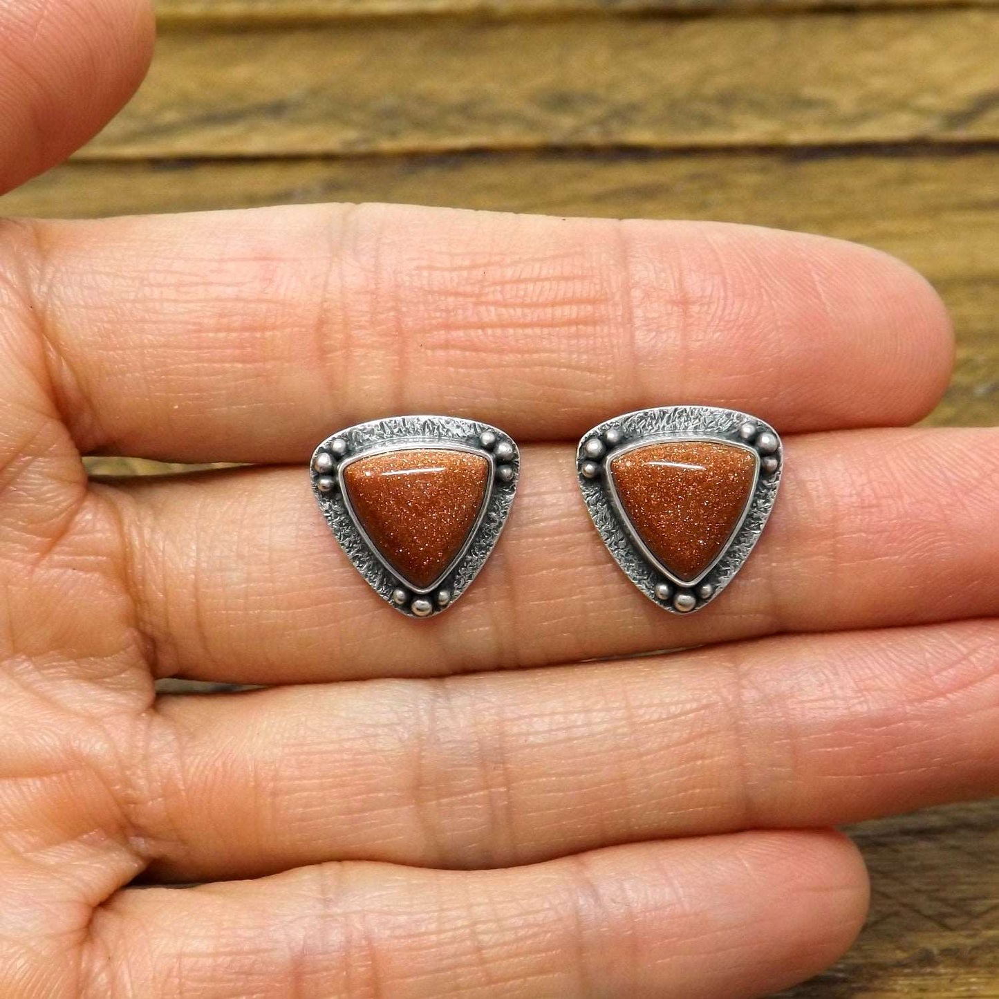 Size reference view of a pair of silver goldstone stud earrings.