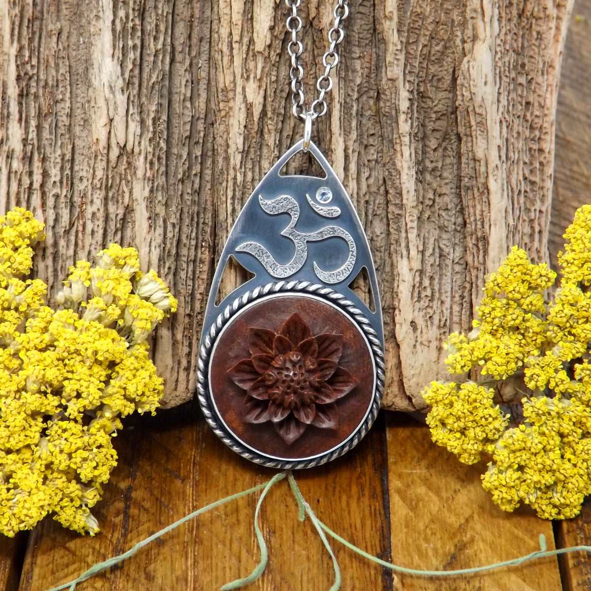 Front view of a sterling silver om necklace featuring a hand carved lotus flower and faceted sapphire gemstone.
