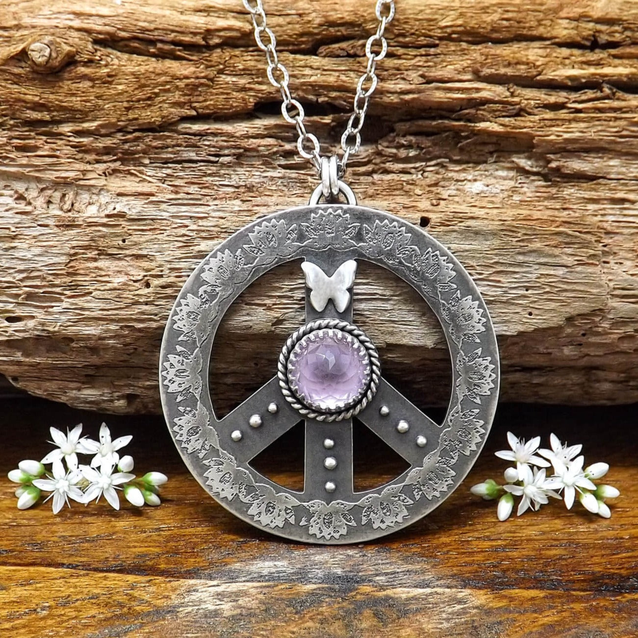 Front view of a sterling silver peace sign necklace with etched lotus flowers, a butterfly, argentium silver granules and amethyst gemstone.