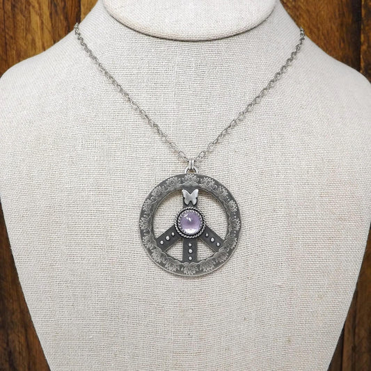 Display bust view of a sterling silver peace sign necklace with etched lotus flowers, a butterfly, argentium silver granules and amethyst gemstone.