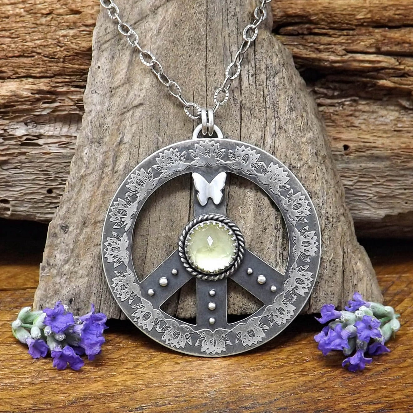 Front view of a sterling silver peace sign necklace with etched lotus flowers, a butterfly, argentium silver granules and a rose cut faceted lemon quartz gemstone.