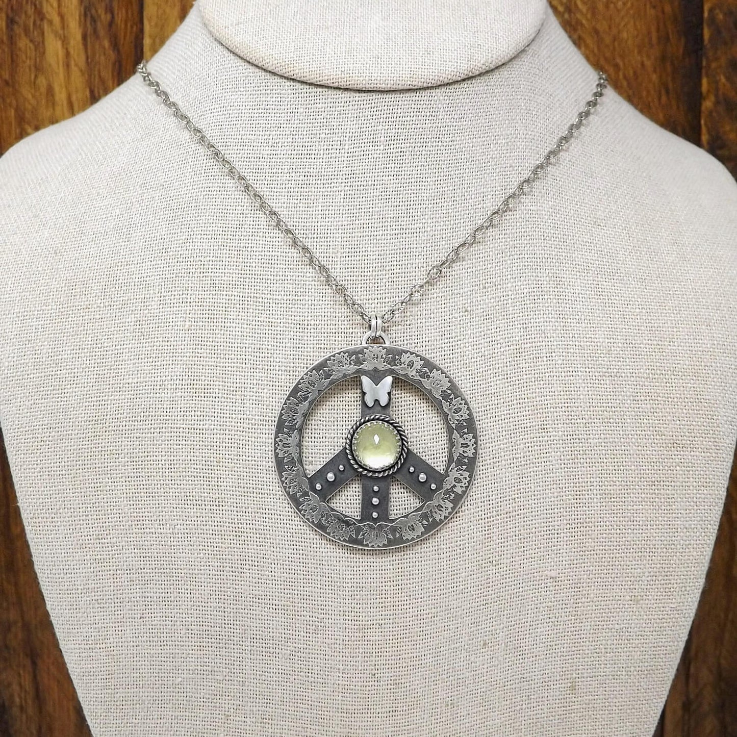 Display bust view of a sterling silver peace sign necklace with etched lotus flowers, a butterfly, argentium silver granules and a rose cut faceted lemon quartz gemstone.