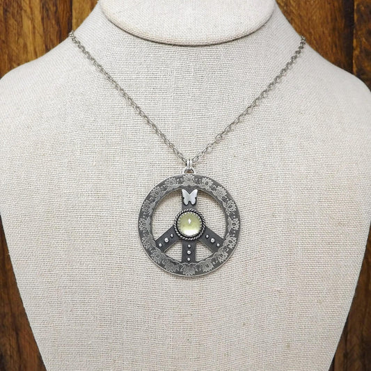 Display bust view of a sterling silver peace sign necklace with etched lotus flowers, a butterfly, argentium silver granules and a rose cut faceted lemon quartz gemstone.