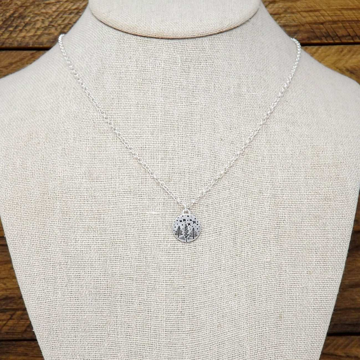 Display bust view of a sterling silver necklace hand-stamped with a starry night forest design.