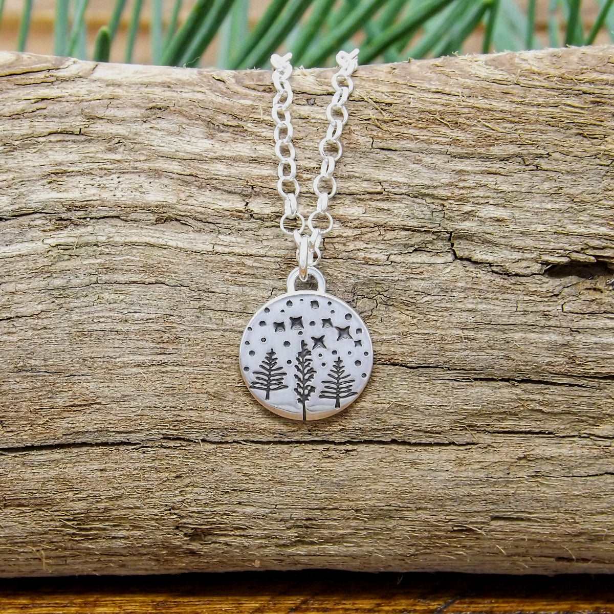 Front view of a sterling silver necklace hand-stamped with a starry night forest design.