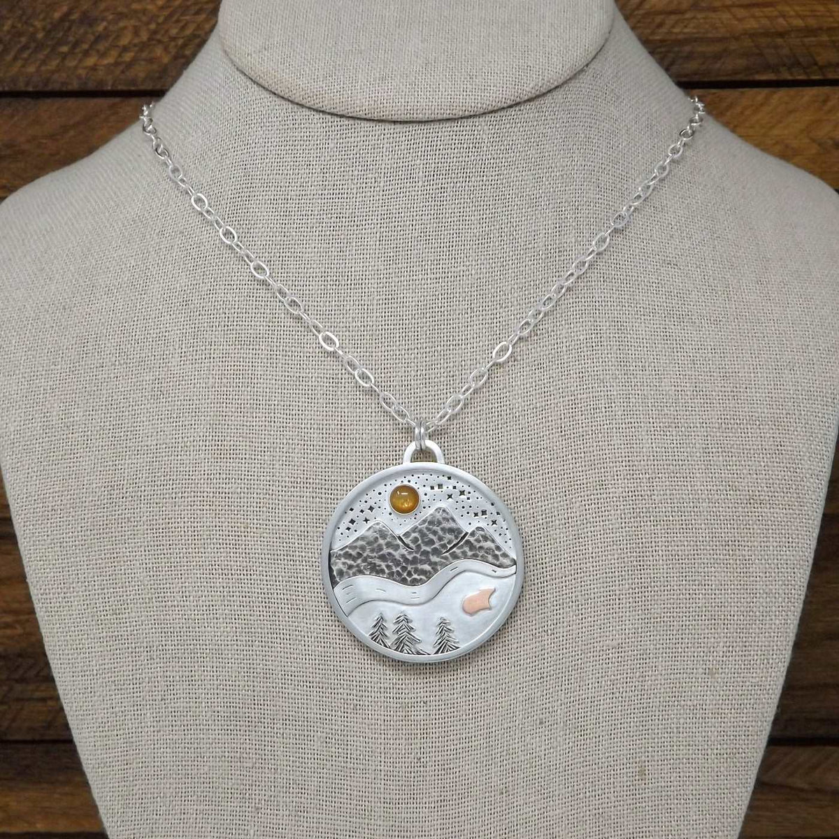 Display bust view of a sterling silver necklace with nature scenery including a gold sunstone gemstone in a starry night sky, mountains, a river, trees, and a tiny copper bear.