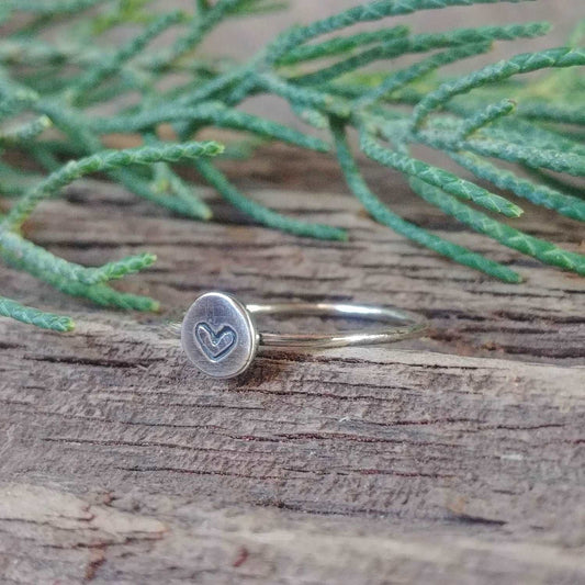 Right angle view of a sterling silver stacking ring with a hand-stamped tiny heart design.