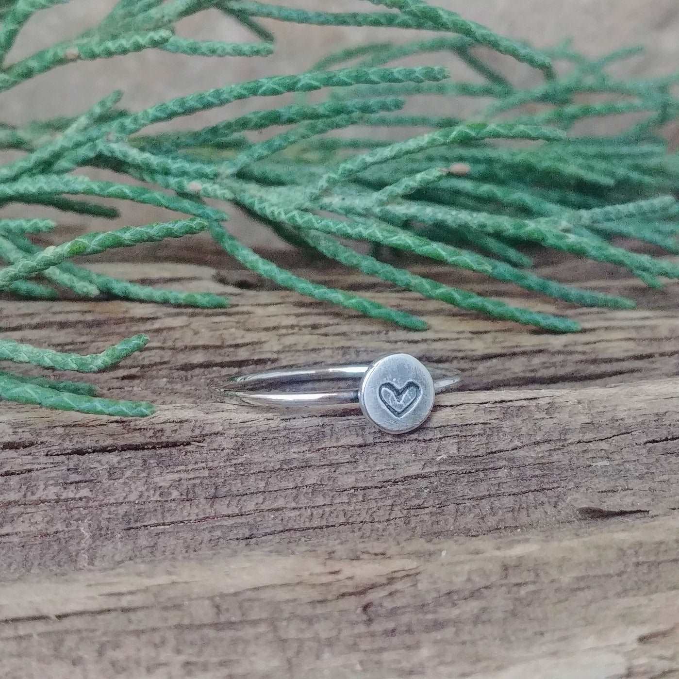 Left angle view of a sterling silver stacking ring with a hand-stamped tiny heart design.
