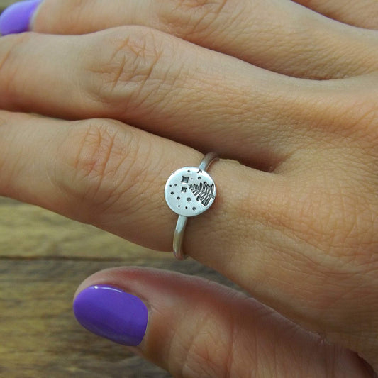 A sterling silver stacking ring with a hand-stamped starry night pine tree design, worn on a hand.
