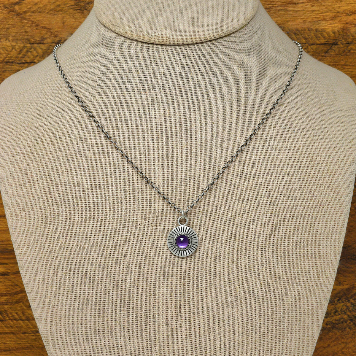 Bust view of a sterling silver sunburst necklace with a rose cut faceted amethyst gemstone.