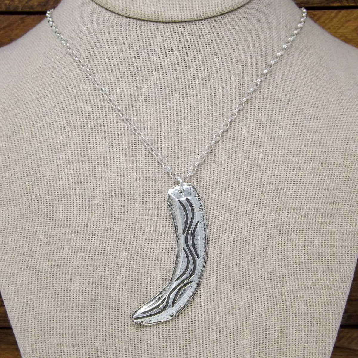 Display bust view of a sterling silver necklace with flowing organic curves and raised textured design made using chasing and repoussé technique.