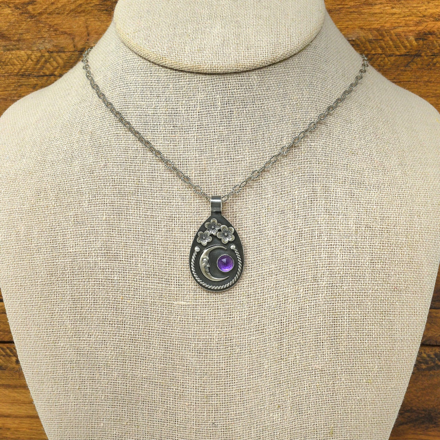 Sterling silver cherry blossom and crescent moon necklace with a rose cut faceted amethyst gemstone displayed on a necklace bust.