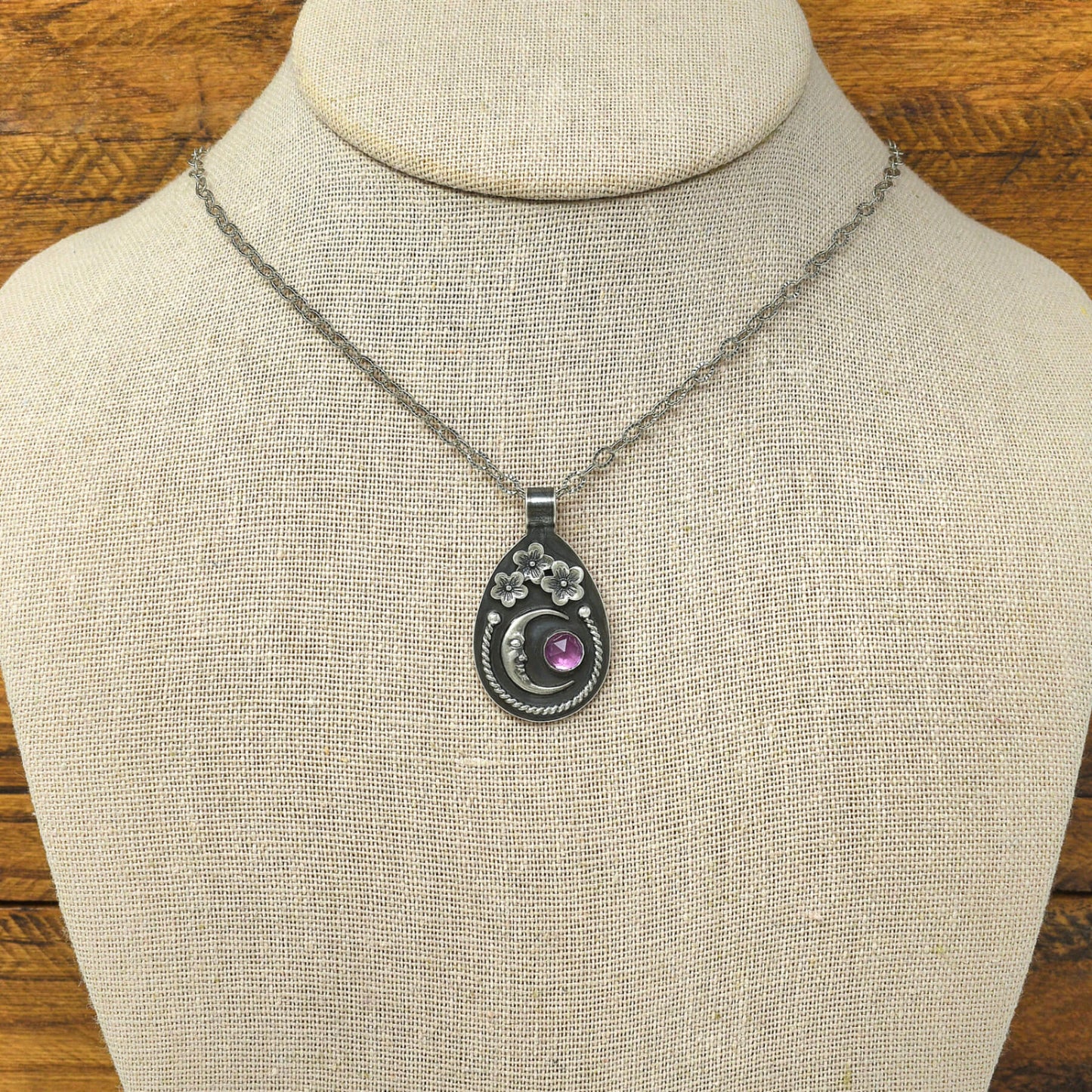 Sterling silver cherry blossom and crescent moon necklace with a rose cut faceted rhodolite garnet shown on a display bust.