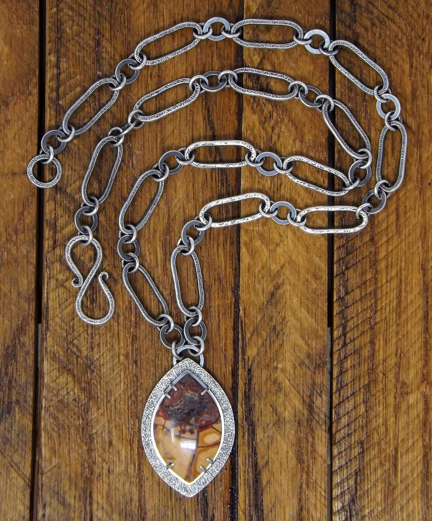 Full view of a sterling silver necklace with a prong set cold mountain jasper gemstone and chunk chain that connects with an s-clasp.