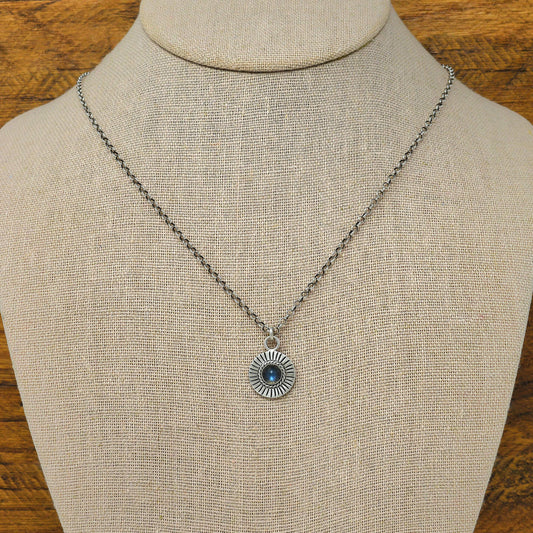 Bust view of a sterling silver sunburst necklace with a rose cut faceted iolite gemstone.