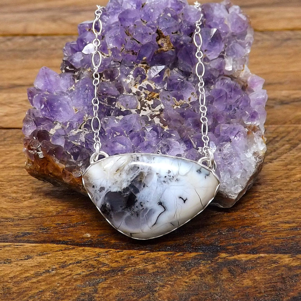 Close up front view of a sterling silver necklace with a dendritic opal gemstone and cut out lotus flower design on the back.