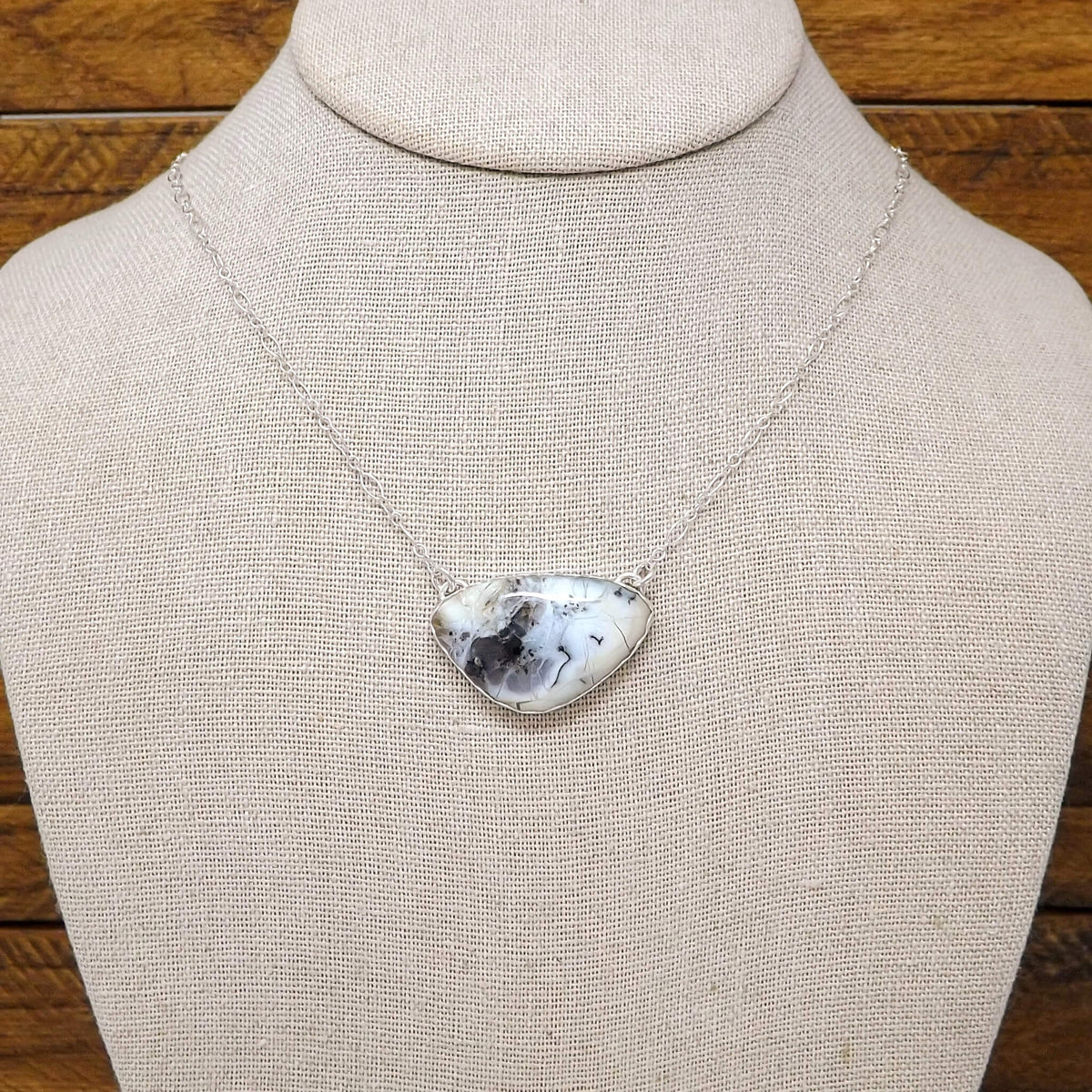 Display bust view of a sterling silver necklace with a dendritic opal gemstone and cut out lotus flower design on the back.