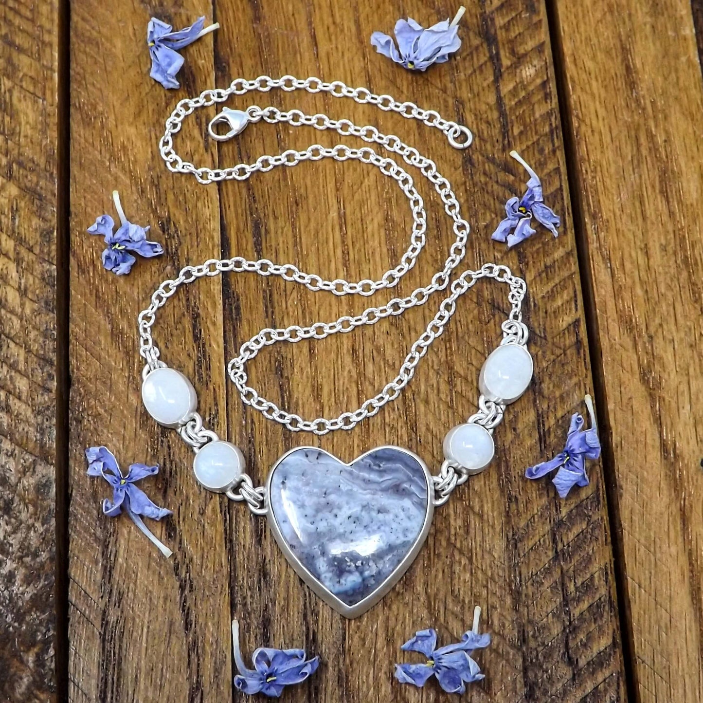Front view of a sterling silver statement necklace featuring a heart shaped luna agate with rainbow moonstone gemstones.