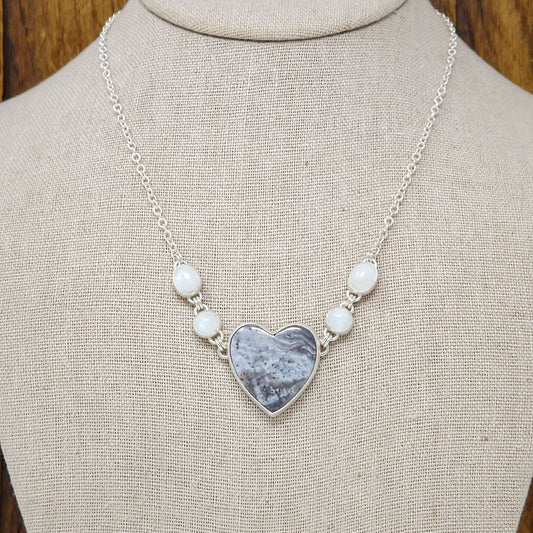 Sterling silver necklace featuring a heart shaped luna agate with rainbow moonstone gemstones on a display bust.