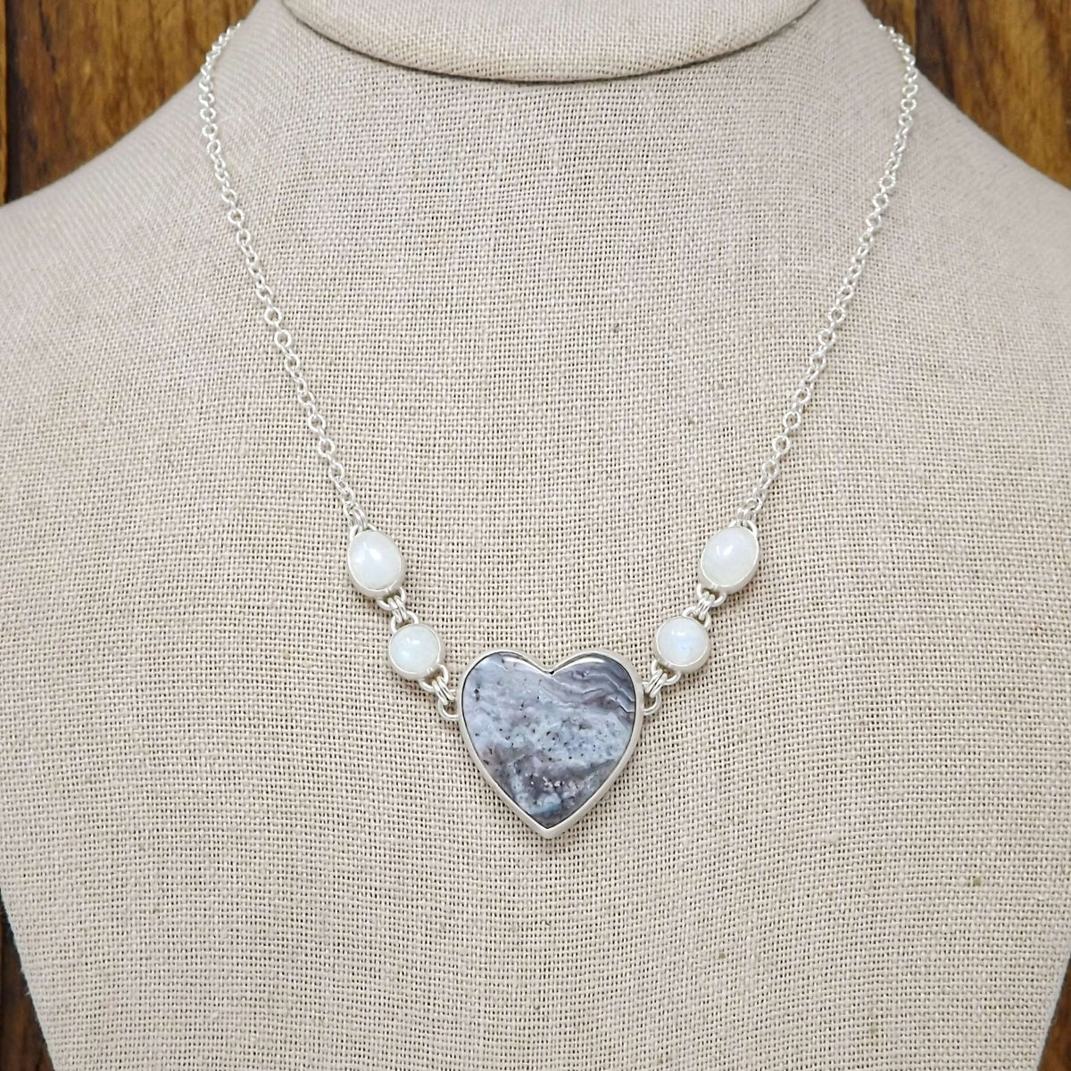Sterling silver necklace featuring a heart shaped luna agate with rainbow moonstone gemstones on a display bust.