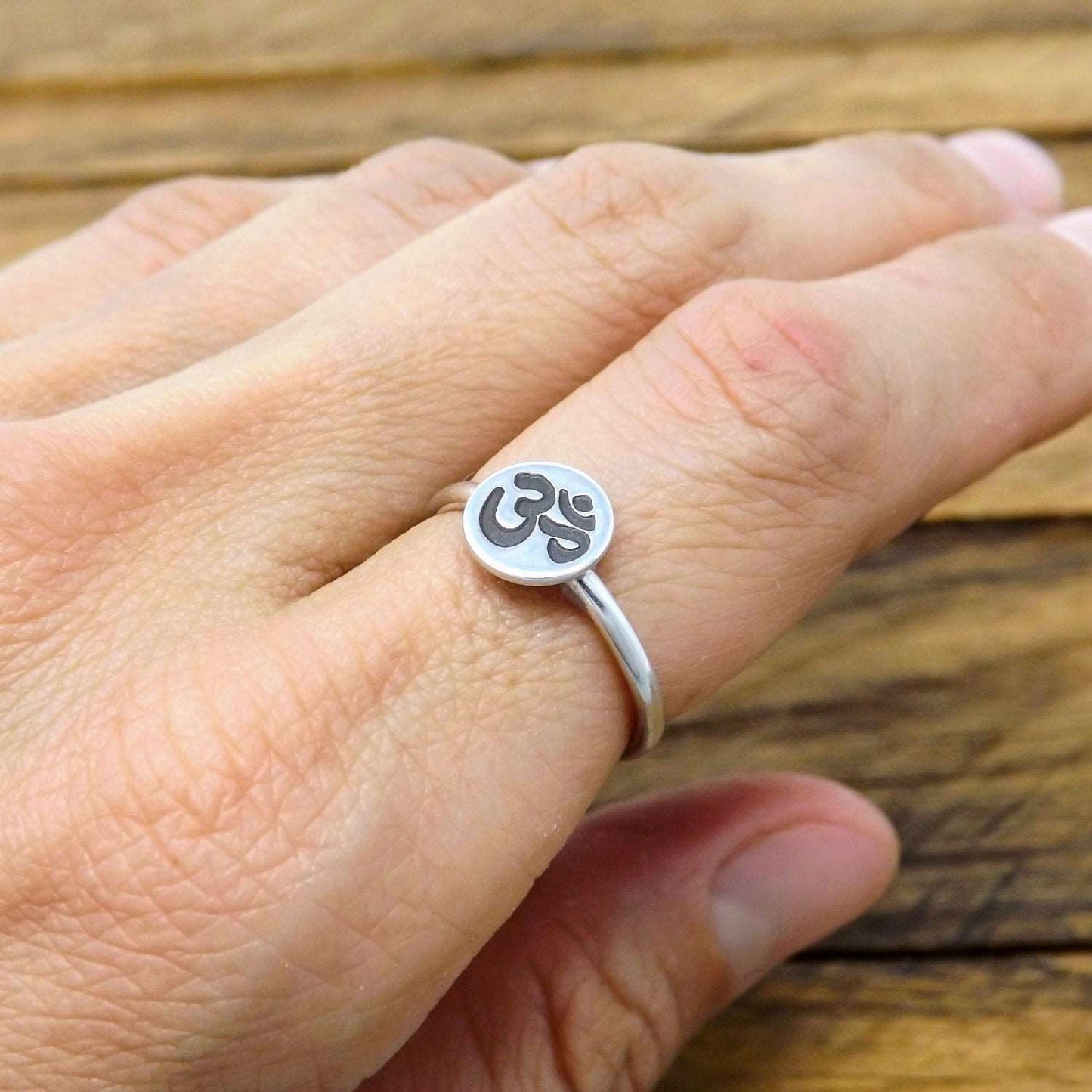 A sterling silver stacking ring with a hand-stamped om symbol design on a person's finger.