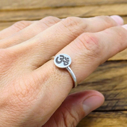 A sterling silver stacking ring with a hand-stamped om symbol design on a person's finger.