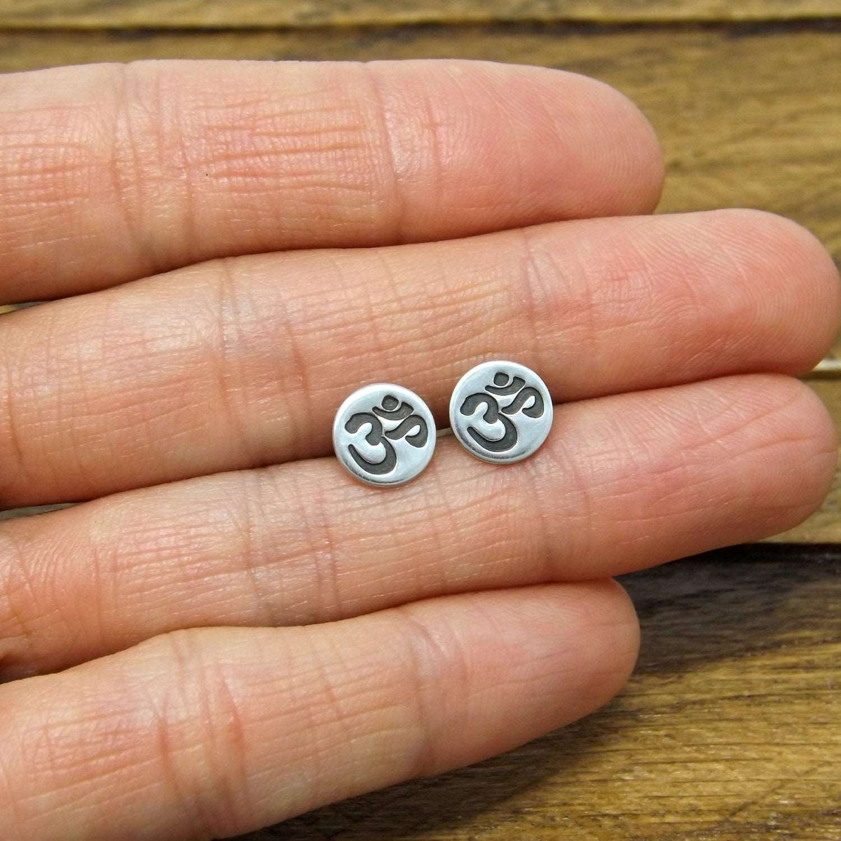 Size reference view of sterling silver stud earrings hand-stamped with om design.