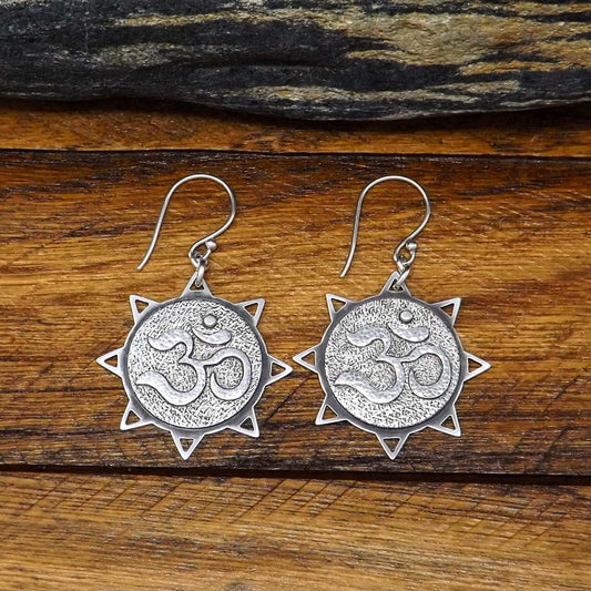 Close up view of a pair of sterling silver sun dangle earrings with om symbols in the center.