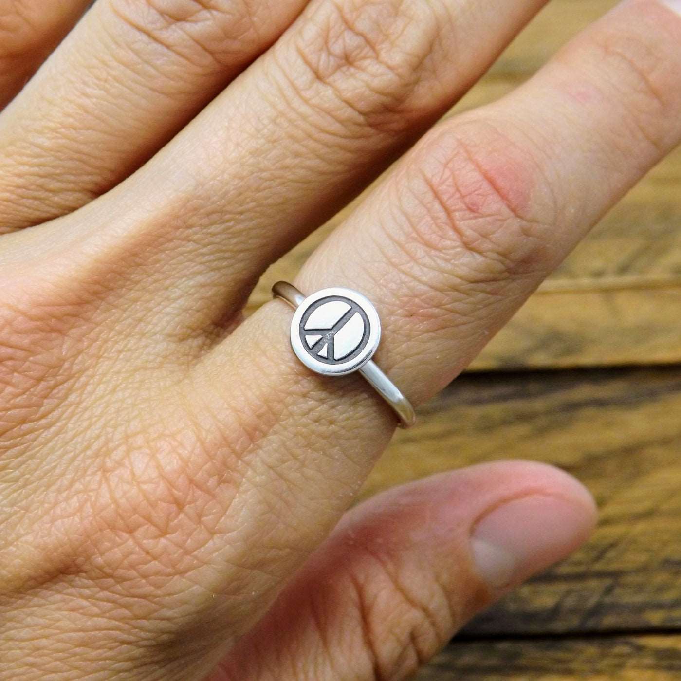 A sterling silver stacking ring with a hand-stamped peace sign design on a person's finger.