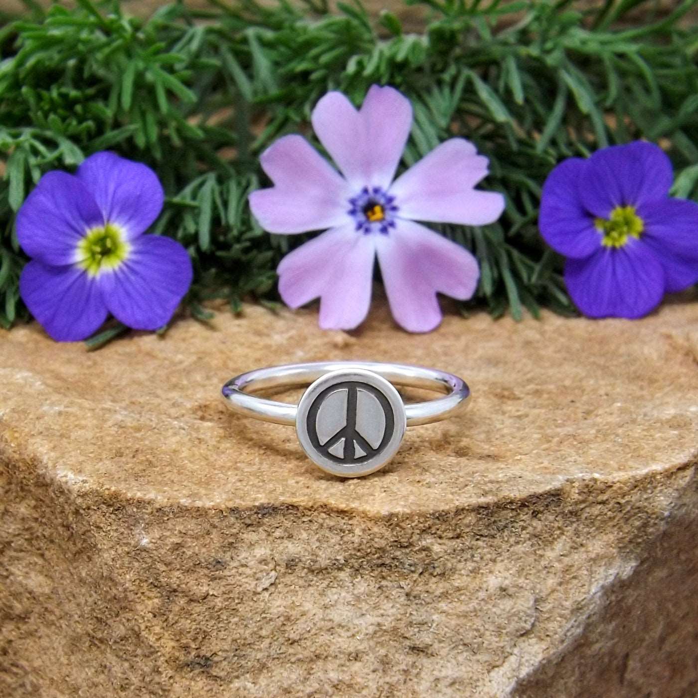 A sterling silver stacking ring with a hand-stamped peace sign design.