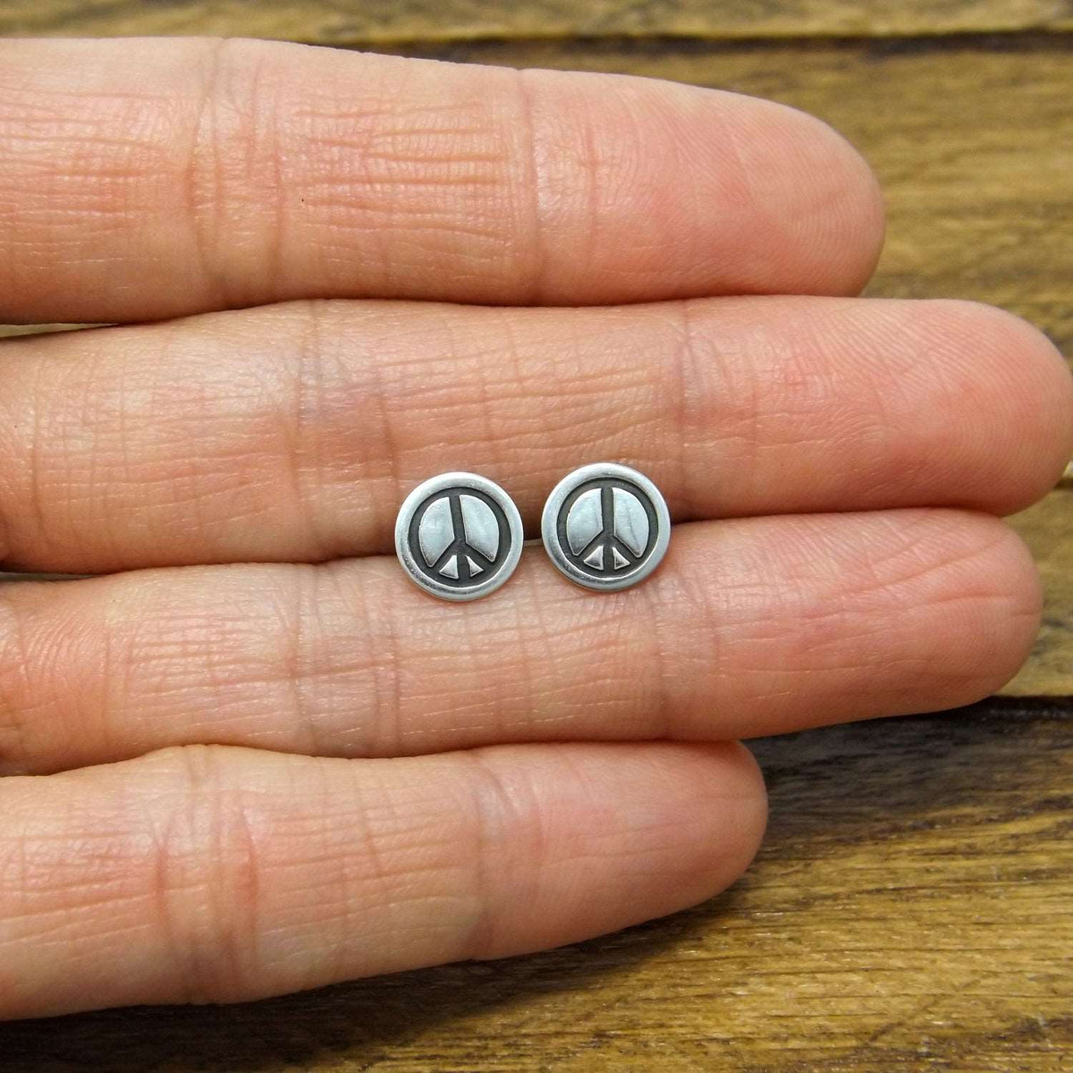 Size reference view of sterling silver stud earrings hand-stamped with peace sign design.