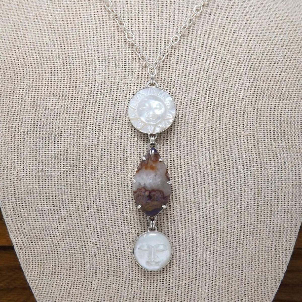 Display bust view of a sterling silver necklace with a prong set purple passion agate and hand carved mother of pearl sun and moon gemstones.