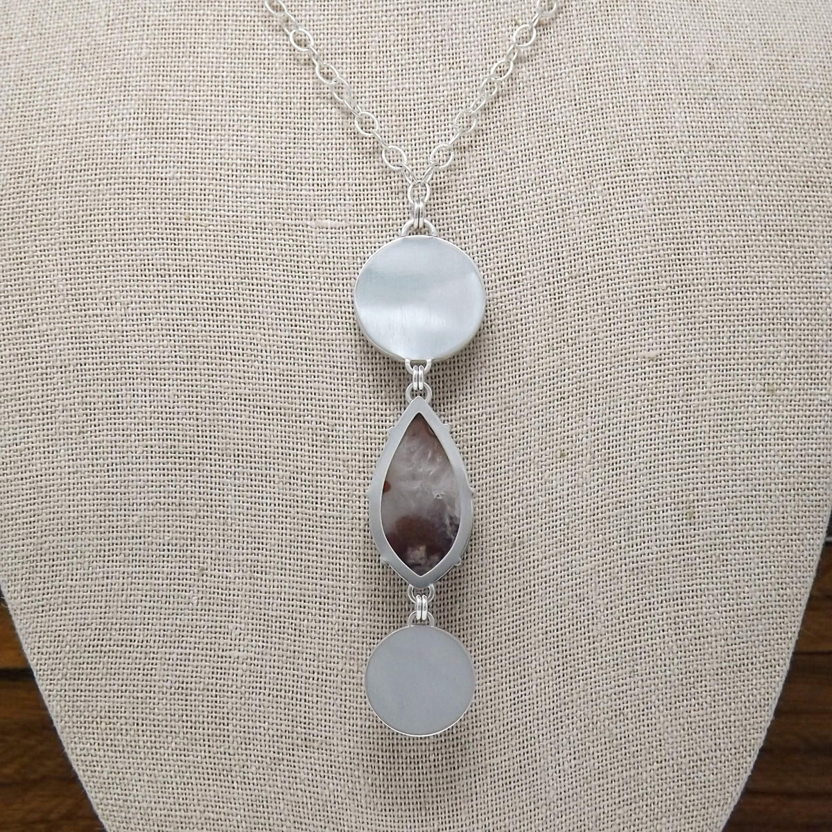 Display bust back view of a sterling silver necklace with a prong set purple passion agate and hand carved mother of pearl sun and moon gemstones.