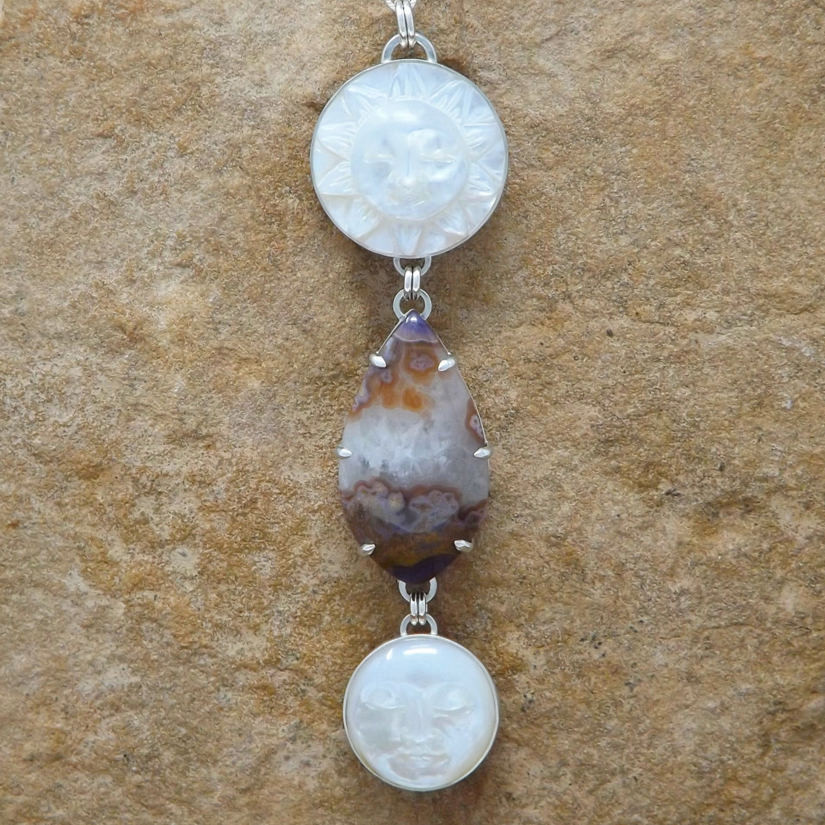 Close up front view of a sterling silver necklace with a prong set purple passion agate and hand carved mother of pearl sun and moon gemstones.