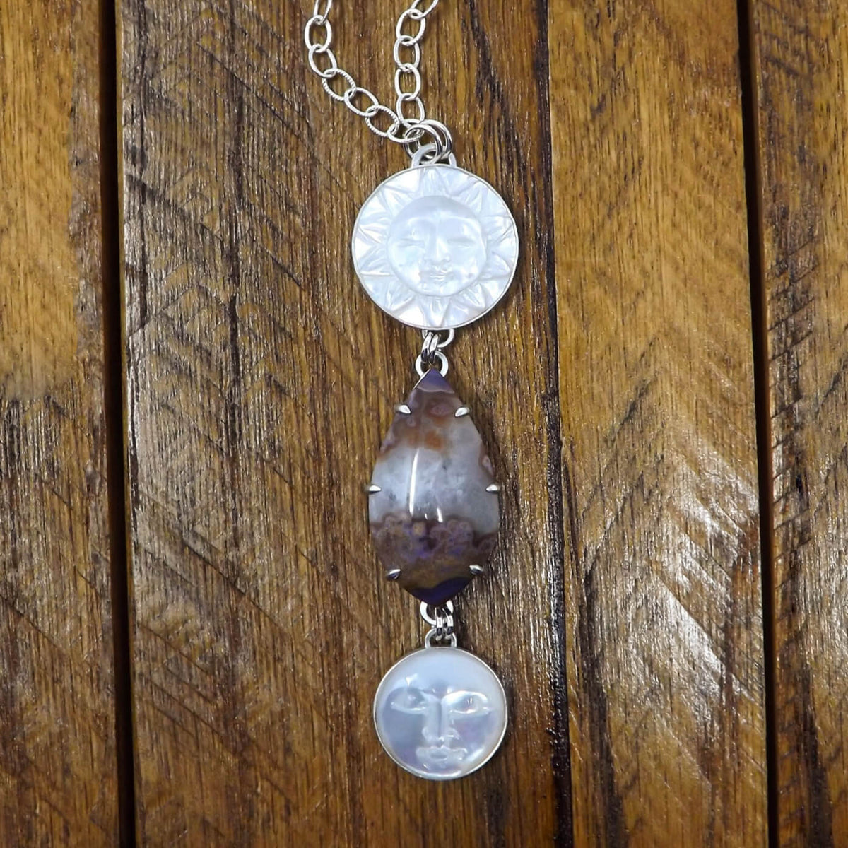 Front view of a sterling silver necklace with a prong set purple passion agate and hand carved mother of pearl sun and moon gemstones.