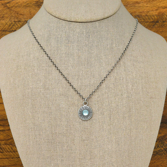 Bust view of a sterling silver sunburst necklace with a rose cut faceted sky blue topaz gemstone.