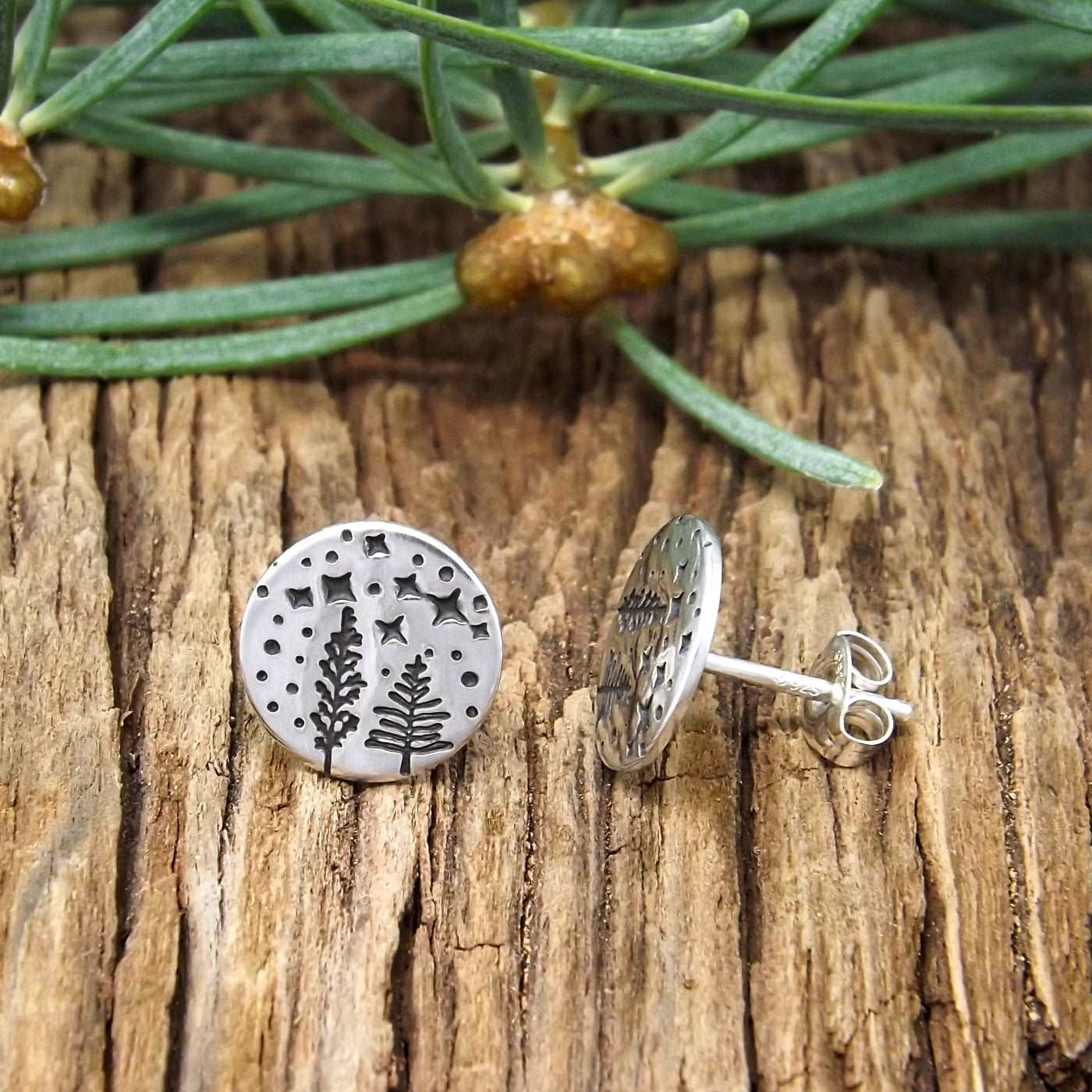 Side view of a pair of sterling silver earrings hand-stamped with a starry night forest design.
